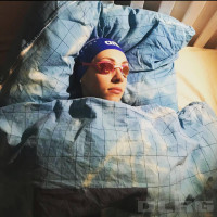 zu sehen ist eine junge Frau mit Schwimmbrille und Badekappe im Bett. Sie träumt vom Training.
